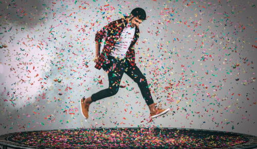 Mid-air shot of handsome young man jumping on trampoline with confetti all around him