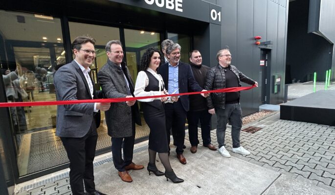 Das Rote Band des Brand Cube wird durchtrennt – und das neue Gebäude auf dem ANWR-Campus damit offiziell eröffnet: (v.l.n.r.): ANWR-Vorstand Tobias Eichmeier, Alexander Böhn, Kreisbeigeordneter des Landkreises Offenbach, die ANWR-Vorstände Martina Novotny und Frank Schuffelen, Mainhausens Bürgermeister Frank Simon und Frank Risse, Geschäftsführer der Werbegemeinschaft des O1. Im Hintergrund: der Vorsitzende des ANWR-Aufsichtsrats, Holger Baierl. (Foto: Redaktion)